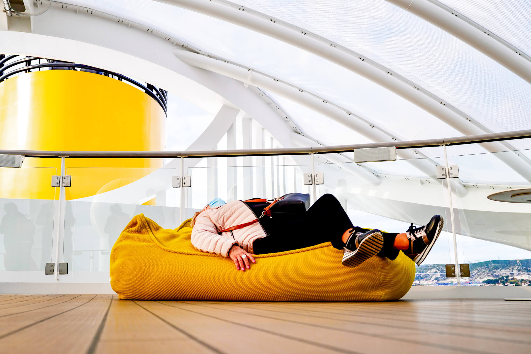 Frau liegt auf Sitzsack an Deck der Costa Smeralda, im Hintergrund der gelbe Schornstein des Kreuzfahrtschiffes
