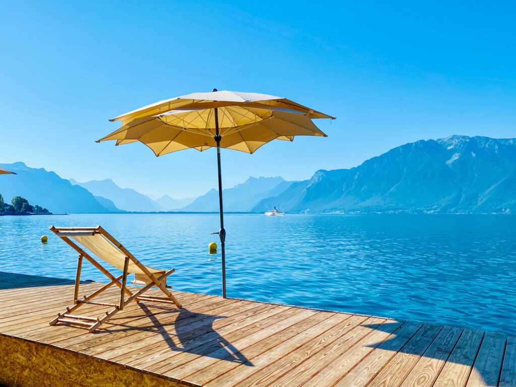 Freier Liegestul unter einem Sonnenschirm am Genfer See