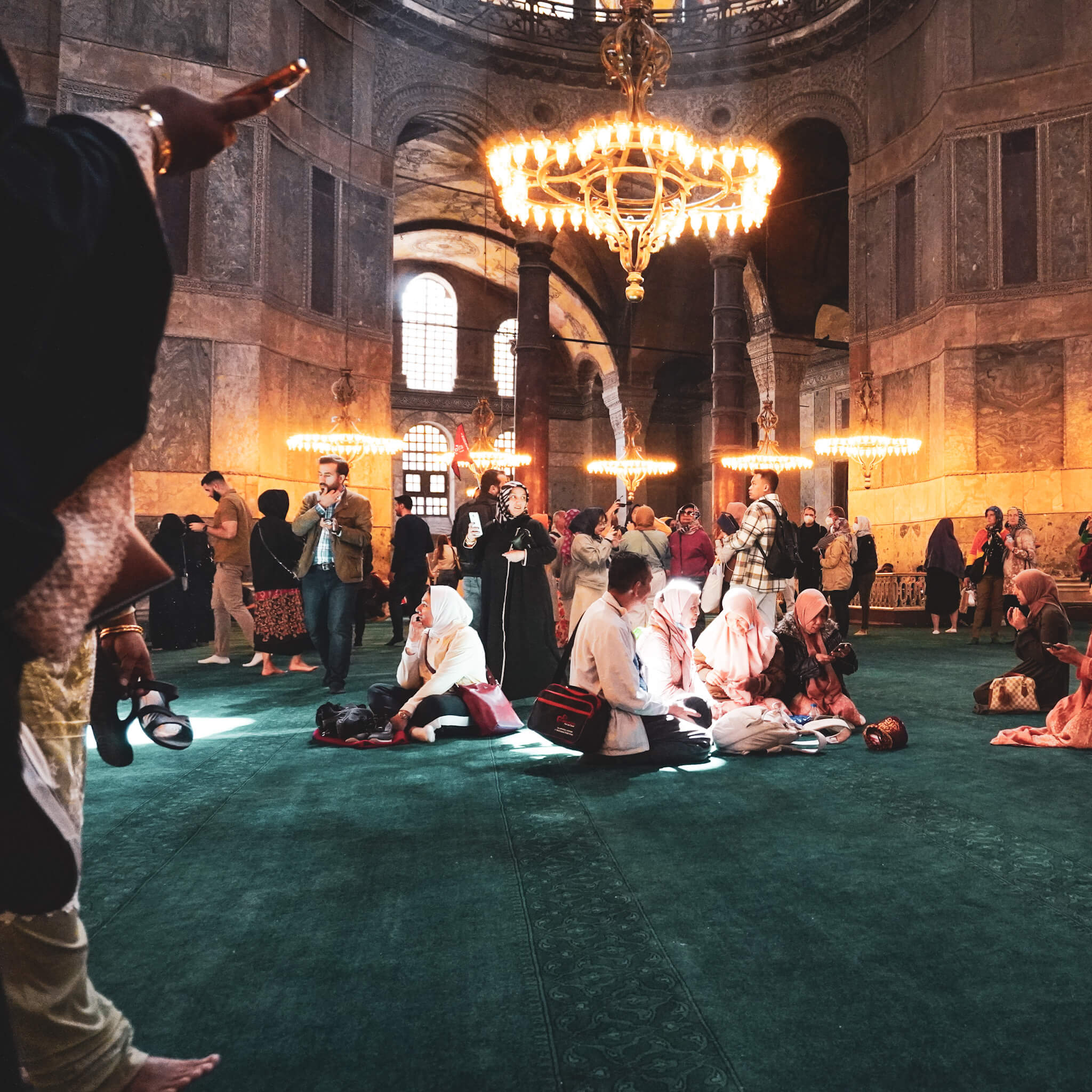 Istanbul, Türkei. Hagia Sofia, innen. Eine Gruppe Menschen sitzt auf dem Teppichboden, Licht fällt auf sie.