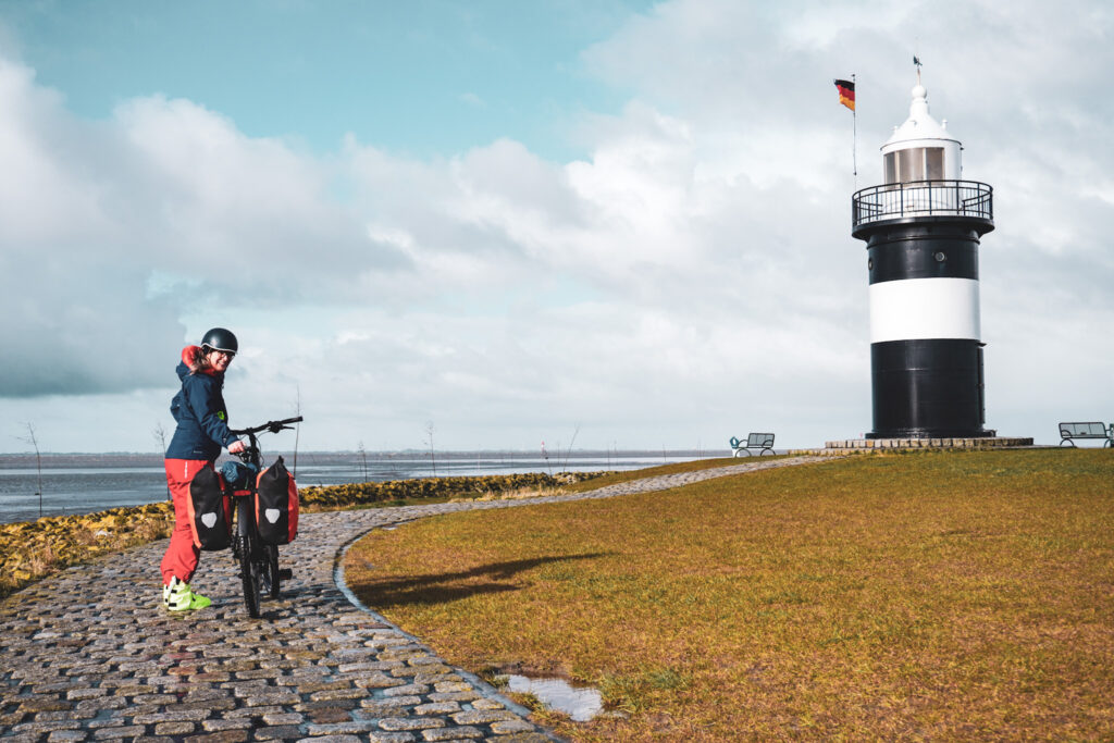 Kirsten Rick in Regenkleidung mit bepacktem Fahrrad am Leuchtturm der Wurster Nordseekueste auf dem Nordseeküstenradweg