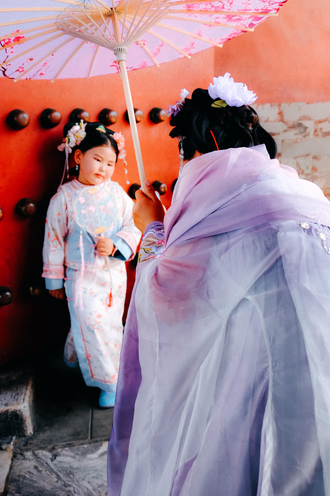 China, Beijing, Kaiserpalast: Mädchen in traditionellem Hanfu-Gewand posiert vor roter Wand und wird fotografiert