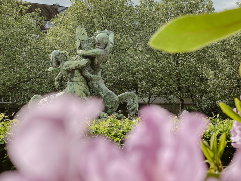 Blick durch Blüten auf die Zentauren des Stuhlmann-Brunnen