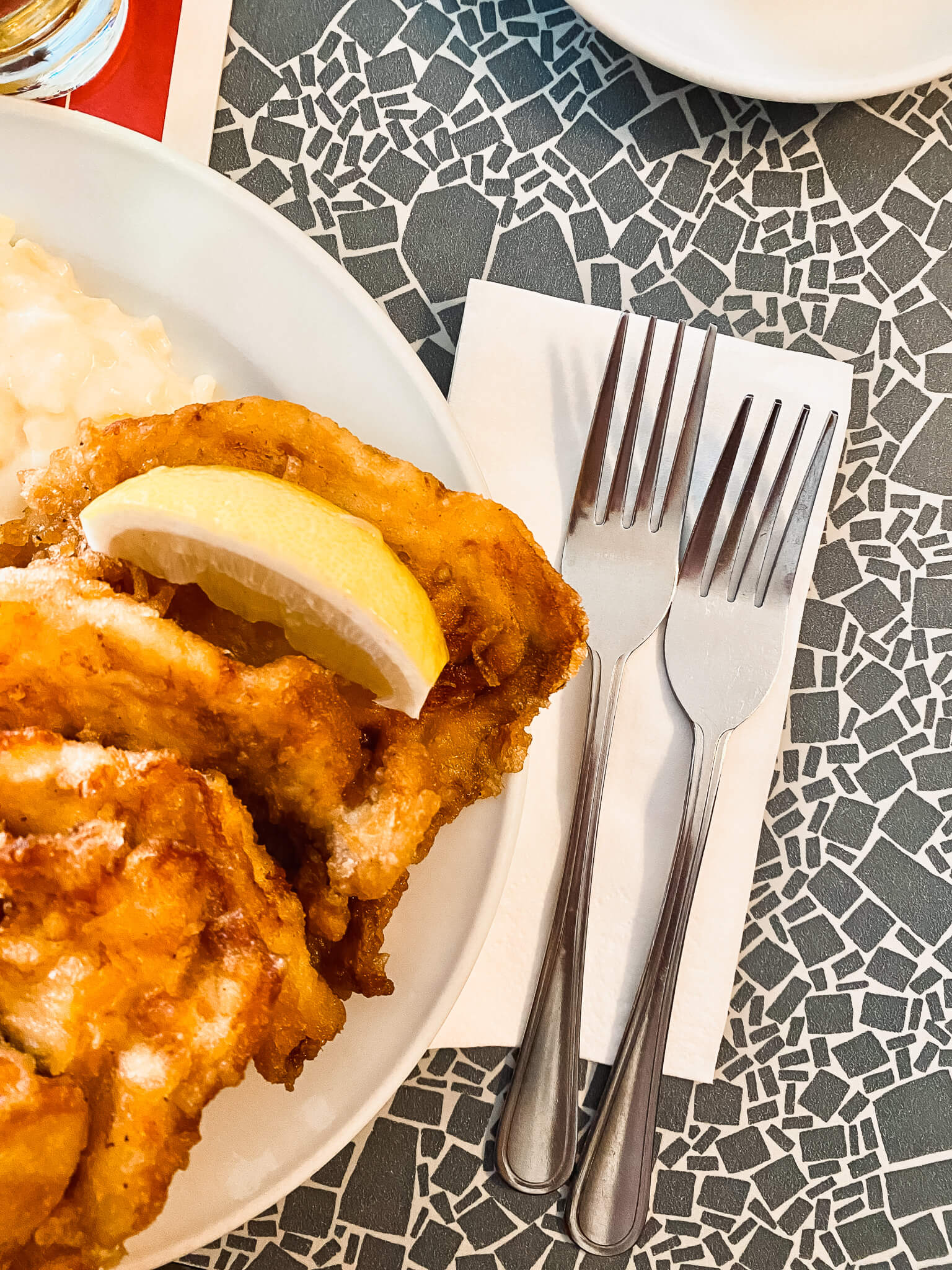 Teller mit Backfisch, daneben zwei Gabeln