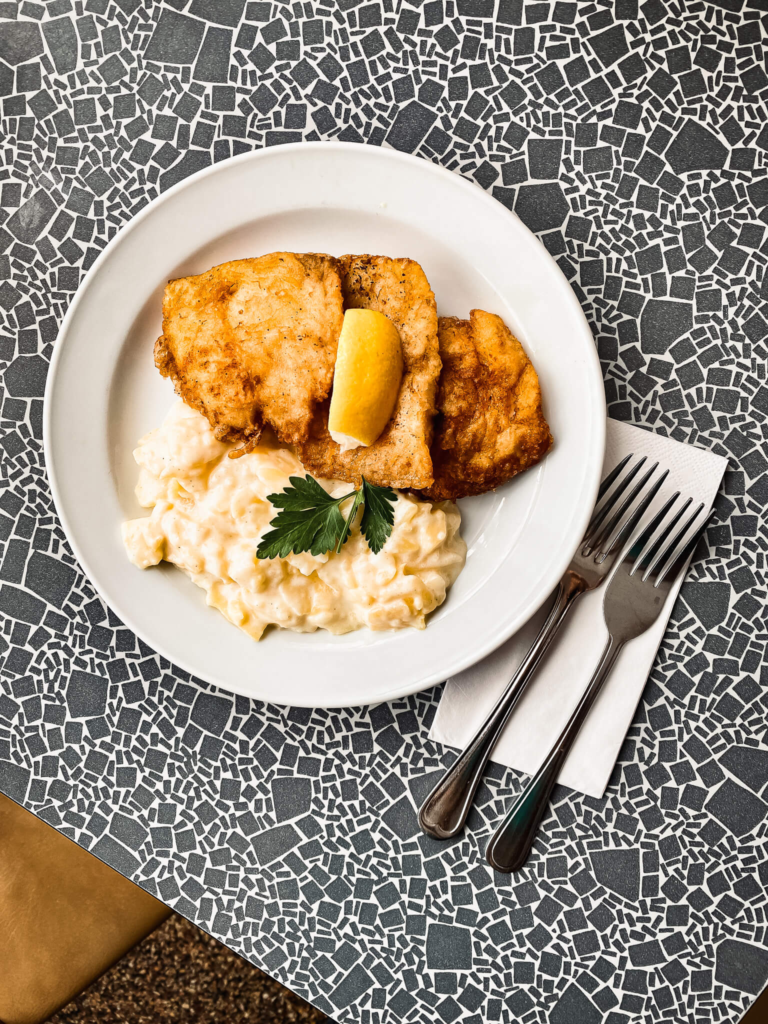 Teller mit Backfisch und Kartoffelsalat, daneben zwei Gabeln
